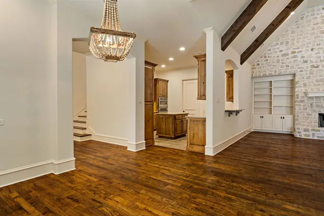 an empty room with wooden floor and way to kitchen
