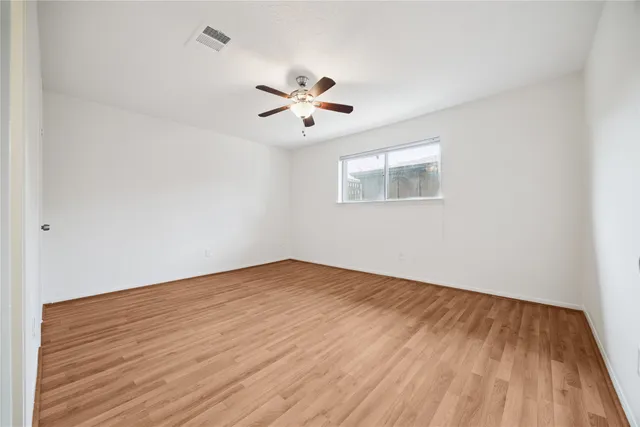 an empty room with wooden floor ceiling fan and windows