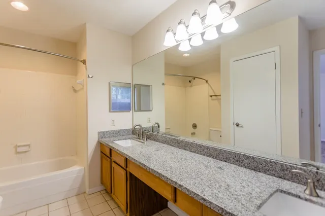 a bathroom with a granite countertop sink a mirror a bathtub and shower