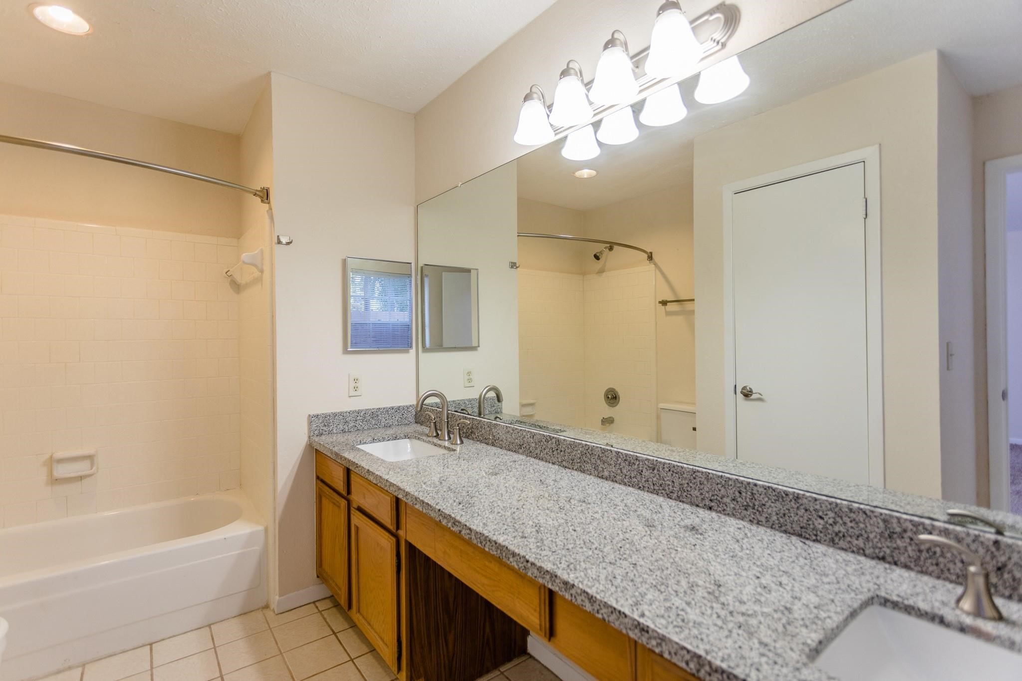 9206 Towerstone Drive Spring, TX 77379 - Photo 5 of 7 a bathroom with a granite countertop sink a mirror a bathtub and shower