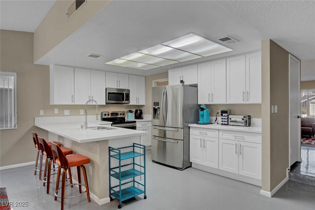 3215 Mountain Spring Road Las Vegas, NV 89146 - Photo 16 of 42 Kitchen with white cabinetry, appliances with stainless steel finishes, a breakfast bar, a peninsula, and a textured ceiling