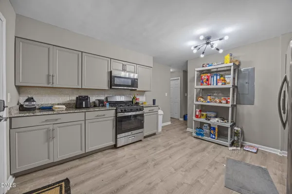 a kitchen with granite countertop a refrigerator a sink dishwasher a stove and white cabinets with wooden floor