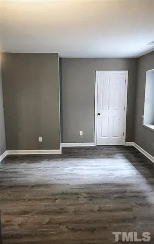 a view of an empty room with wooden floor and window