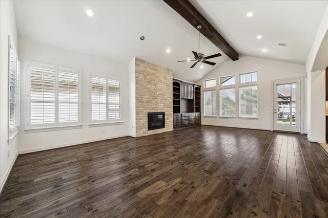 an empty room with wooden floor fire place and windows