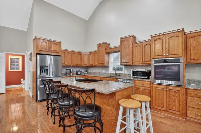 a kitchen with stainless steel appliances granite countertop a stove top oven a refrigerator a sink and chairs with wooden floor