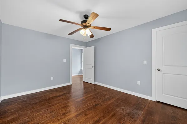 a view of an empty room with wooden floor and a ceiling fan