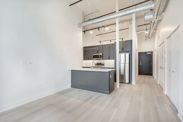 a room with stainless steel appliances kitchen island granite countertop a refrigerator and a sink