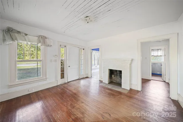 an empty room with wooden floor fireplace and windows