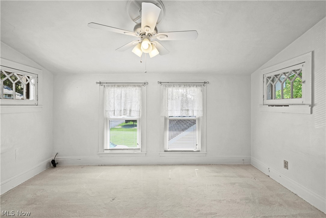 503 Ravenna Road Newton Falls, OH 44444 - Photo 13 of 34 Carpeted interior space featuring a ceiling fan with integrated lighting, two rectangular windows with sheer curtains, and two smaller arched windows with decorative grilles