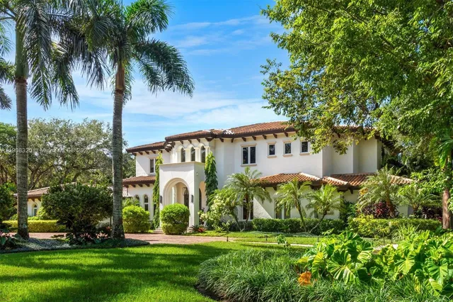 a view of a white house with a big yard and potted plants and large trees