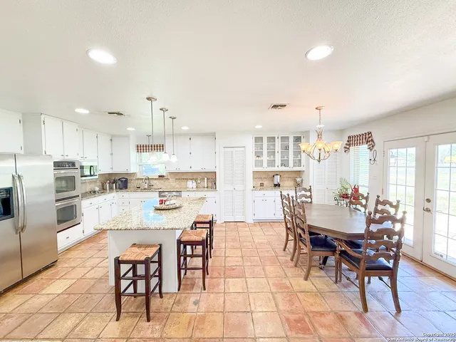 a kitchen with stainless steel appliances kitchen island granite countertop a dining table chairs and a refrigerator