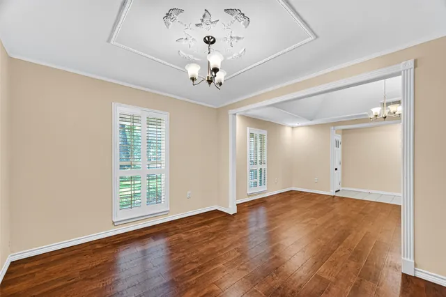 an empty room with wooden floor chandelier fan and windows