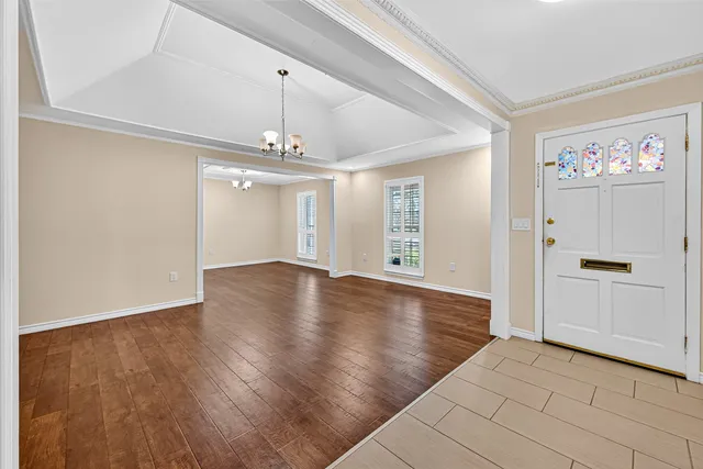 an empty room with wooden floor chandelier and windows