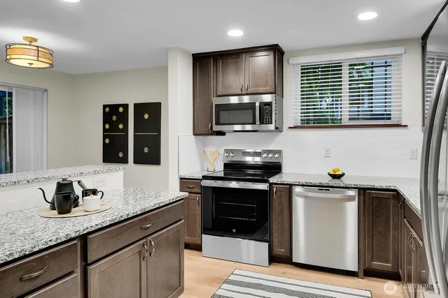 a kitchen with granite countertop stainless steel appliances a sink cabinets and wooden floor