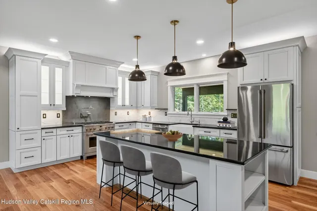 a kitchen with stainless steel appliances granite countertop a stove a sink a refrigerator a center island and chairs with wooden floor