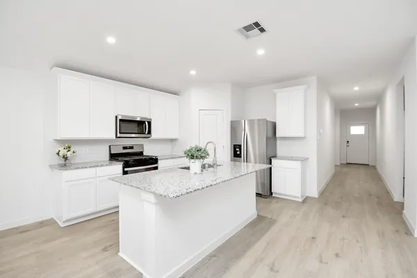 a large white kitchen with stainless steel appliances a refrigerator a stove a sink dishwasher and white cabinets with wooden floor