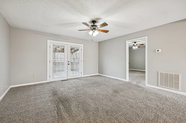 an empty room with chandelier fan and windows