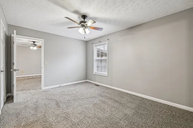an empty room with a chandelier fan and windows
