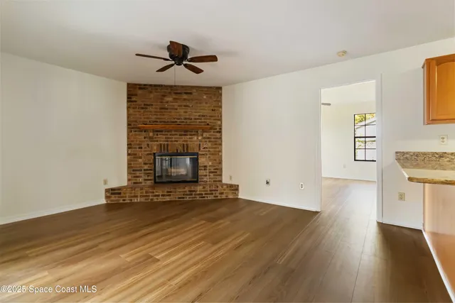 a view of an empty room with wooden floor fireplace and a window