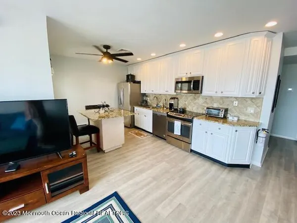 a kitchen with stainless steel appliances a stove a sink a microwave a refrigerator a stove and white cabinets with wooden floor