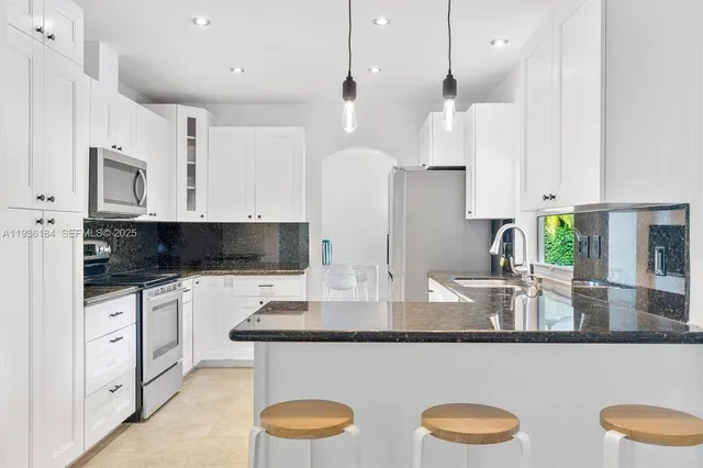 a kitchen with stainless steel appliances granite countertop a stove a sink a microwave a refrigerator and white cabinets with wooden floor