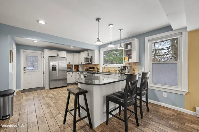 a kitchen with stainless steel appliances kitchen island granite countertop a dining table chairs and white cabinets