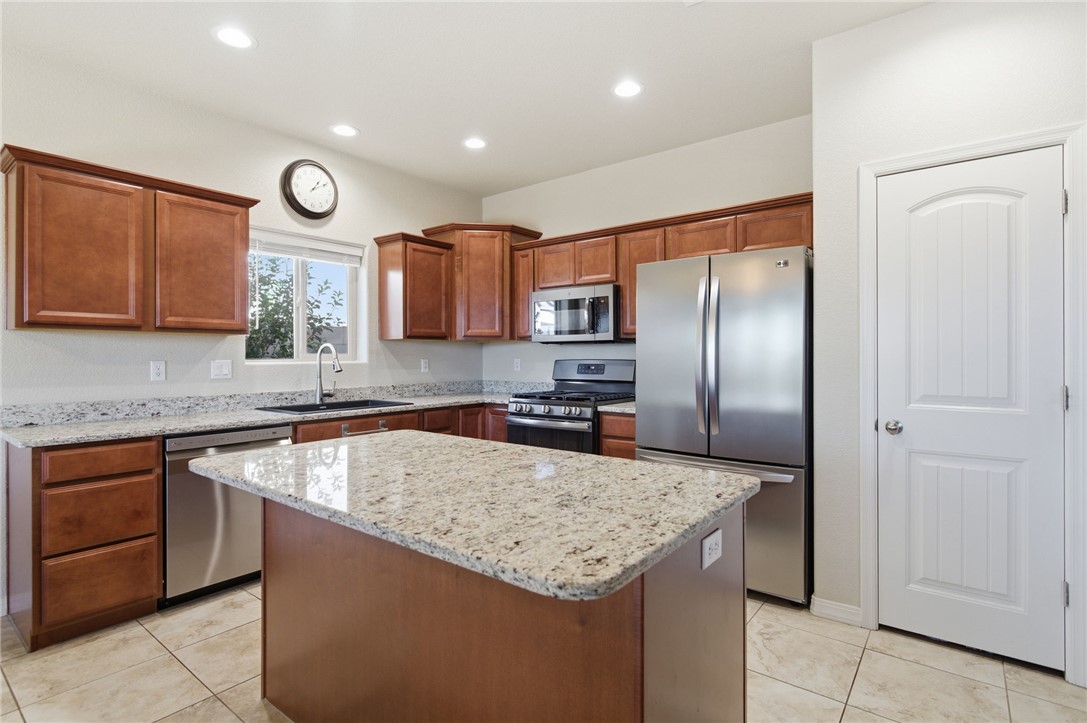 4745 East Old W Road Kingman, AZ 86401 - Photo 10 of 37 Kitchen featuring appliances with stainless steel finishes, light stone counters, a center island, brown cabinetry, and light tile patterned floors