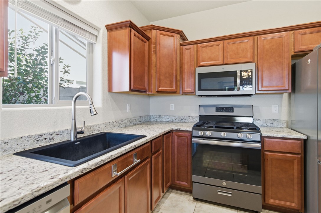 4745 East Old W Road Kingman, AZ 86401 - Photo 11 of 37 Kitchen featuring stainless steel appliances, light stone counters, brown cabinets, and light tile patterned flooring