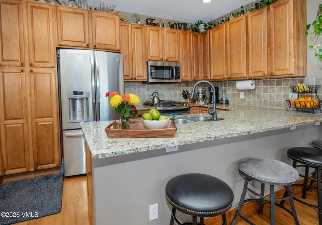 a kitchen with stainless steel appliances granite countertop a refrigerator a sink a stove a dining table and chairs with wooden floor