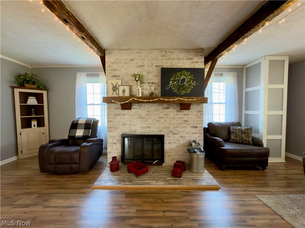 17377 Murphy Road Amesville, OH 45711 - Photo 5 of 43 Living room featuring beamed ceiling, wood finished floors, a textured ceiling, a brick fireplace, and plenty of natural light