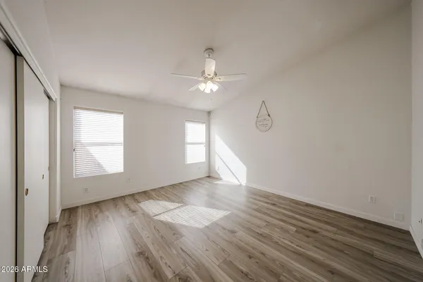 an empty room with wooden floor chandelier fan and windows