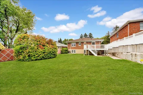 a view of a white house in front of a big yard with plants and large trees