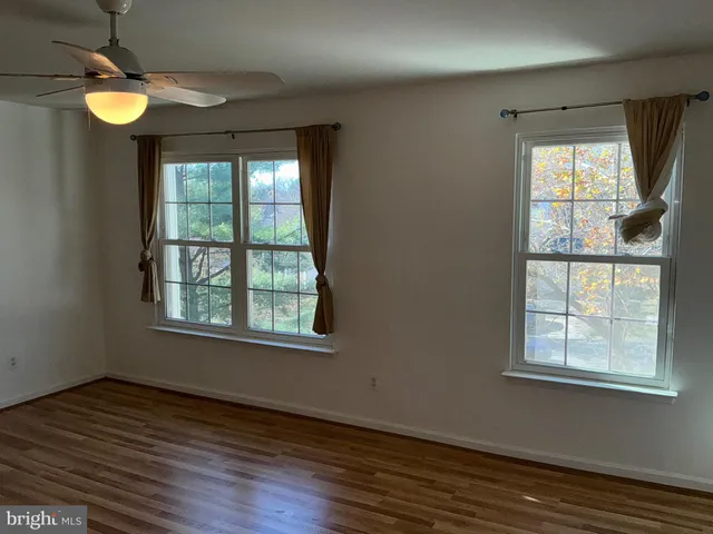 an empty room with wooden floor fan and windows