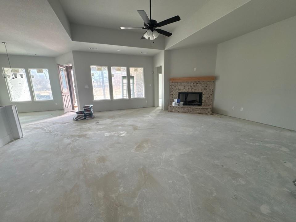 152 Oak Grv Way Springtown, TX 76082 - Photo 5 of 10 Unfurnished living room featuring a brick fireplace, unfinished concrete flooring, a tray ceiling, and healthy amount of natural light