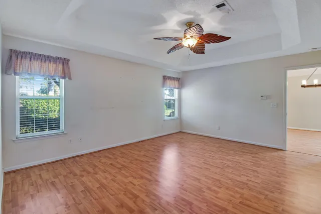 an empty room with wooden floor chandelier fan and windows