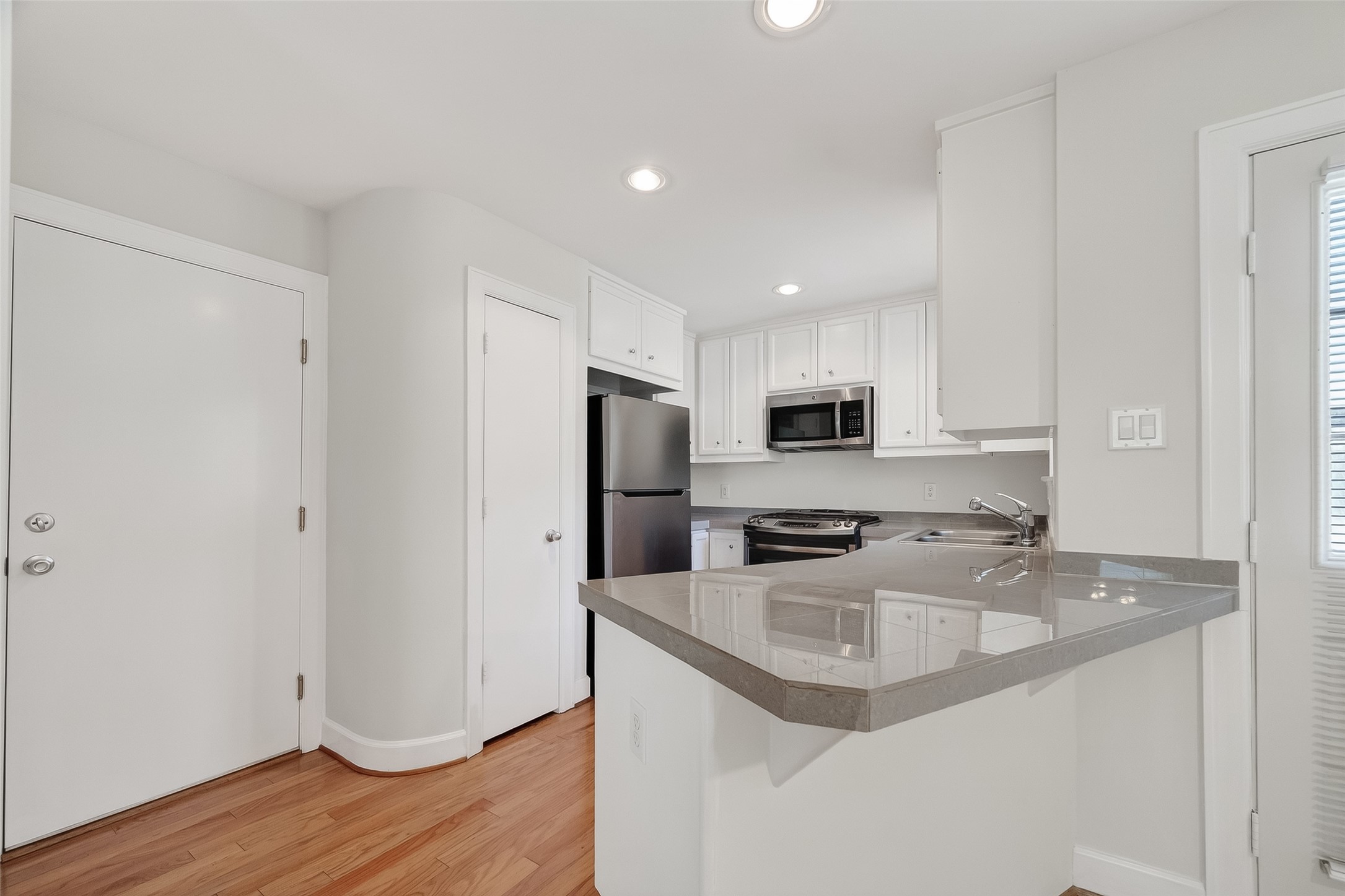 5951 S Loop East, Unit 47 Houston, TX 77033 - Photo 14 of 37 This photo showcases a modern kitchen with sleek white cabinets, stainless steel appliances, and a polished countertop with an integrated sink. The space features hardwood floors and ample lighting, creating a bright and welcoming atmosphere.