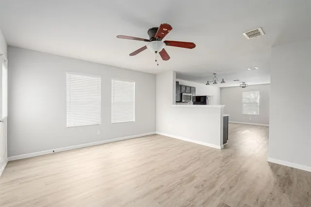a view of a livingroom with wooden floor a ceiling fan and windows