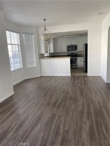 an empty room with wooden floor and kitchen view