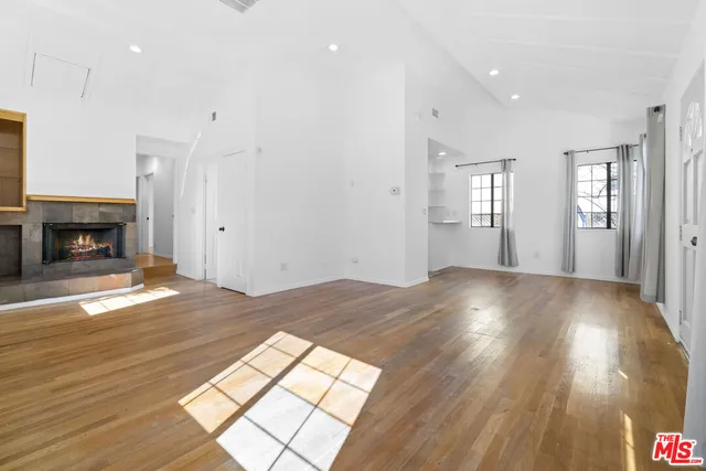 an empty room with wooden floor fireplace and windows