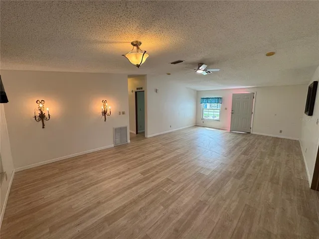 an empty room with wooden floor chandelier fan and windows