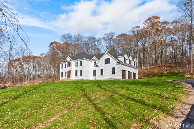 a view of a white house next to a yard with big trees