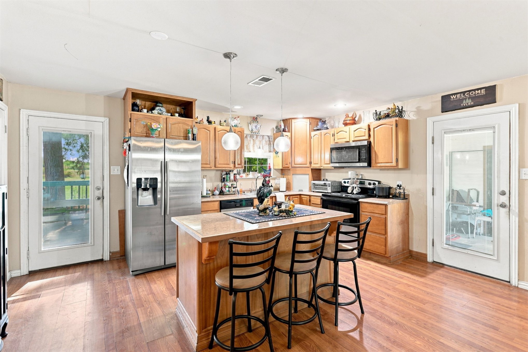 208 West Umstead Colbert, OK 74733 - Photo 14 of 25 Kitchen featuring wood-finish flooring, a central island with a breakfast bar, light wood cabinetry, stainless steel appliances, and two glass-paneled exterior doors