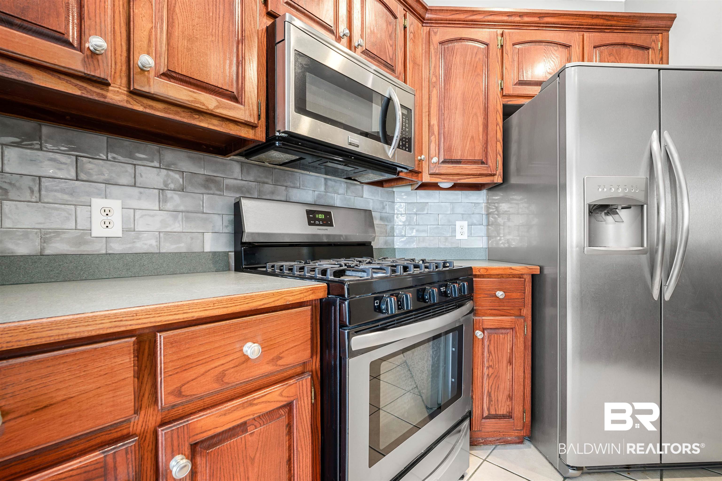 615 Summerlake Place Mobile, AL 36608 - Photo 9 of 35 Kitchen with stainless steel appliances, light countertops, brown cabinetry, tasteful backsplash, and light tile patterned floors