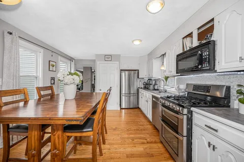 a kitchen with stainless steel appliances granite countertop a stove top oven a sink dishwasher a dining table and chairs with wooden floor