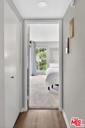 a view of a hallway to a bedroom with wooden floor and a window