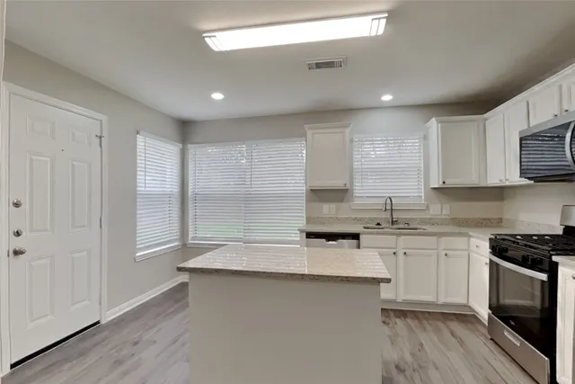 a kitchen with stainless steel appliances granite countertop a sink a stove a microwave a refrigerator a cabinets and wooden floor