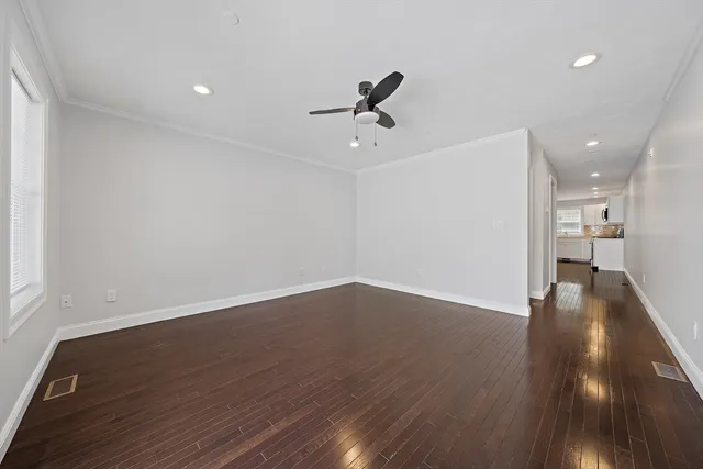 a view of an empty room with wooden floor and a ceiling fan