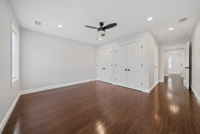 a view of an empty room with wooden floor and a ceiling fan