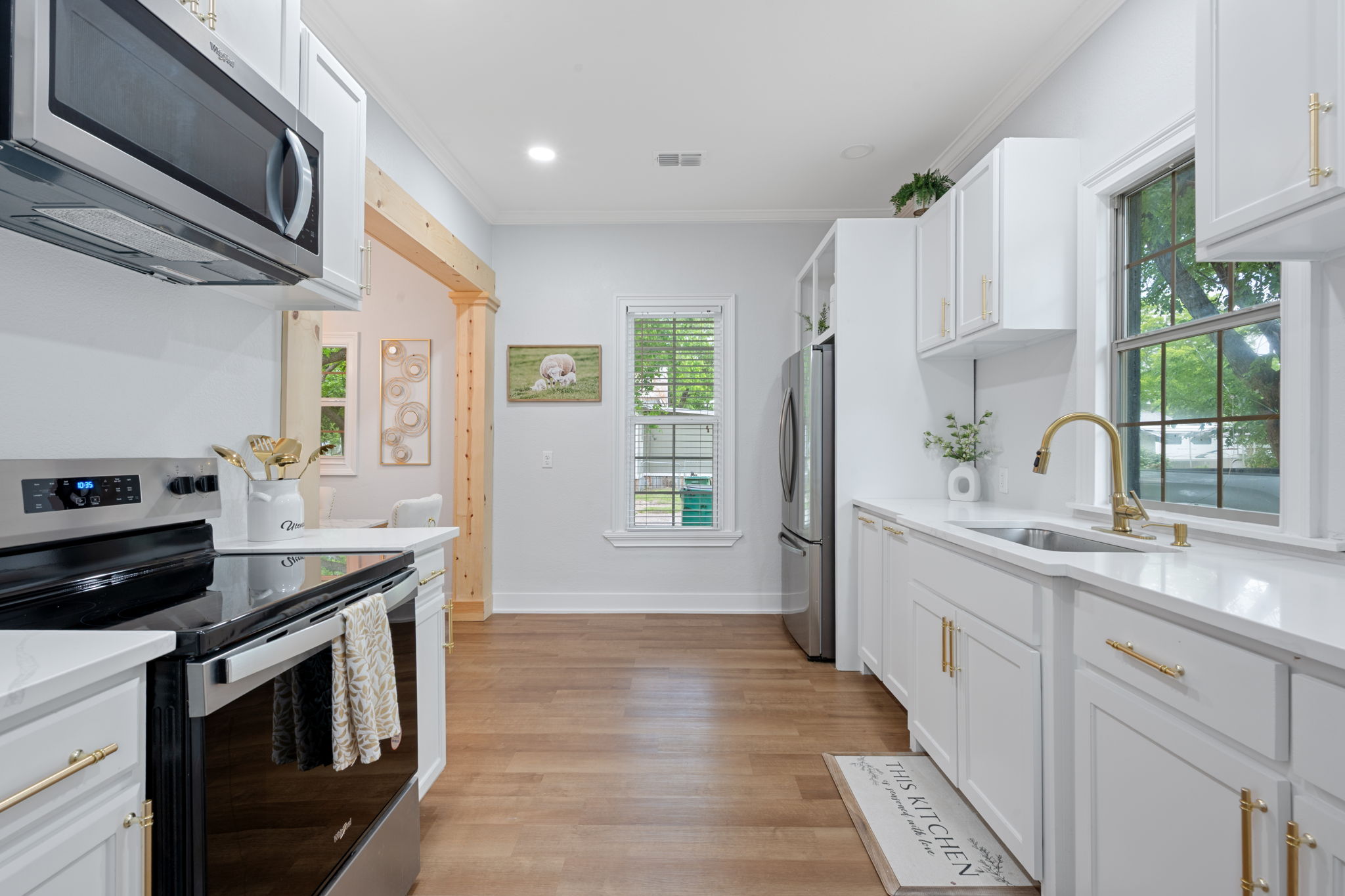 602 East 6th Street Cameron, TX 76520 - Photo 17 of 40 Bright kitchen featuring white cabinetry with gold-tone hardware, a stainless steel sink with gold-tone faucet, white countertops, and wood-finish flooring