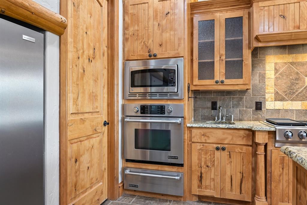 2085 Switzer Road Sanger, TX 76266 - Photo 11 of 39 Kitchen featuring stainless steel appliances, wood-finish cabinetry, a tiled backsplash, and granite countertops